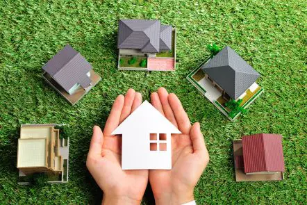 Hands holding house cutout among mini house models