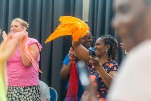 A person dances with an orange streamer, waving it in the air, surrounded by others on the dance floor - relationships