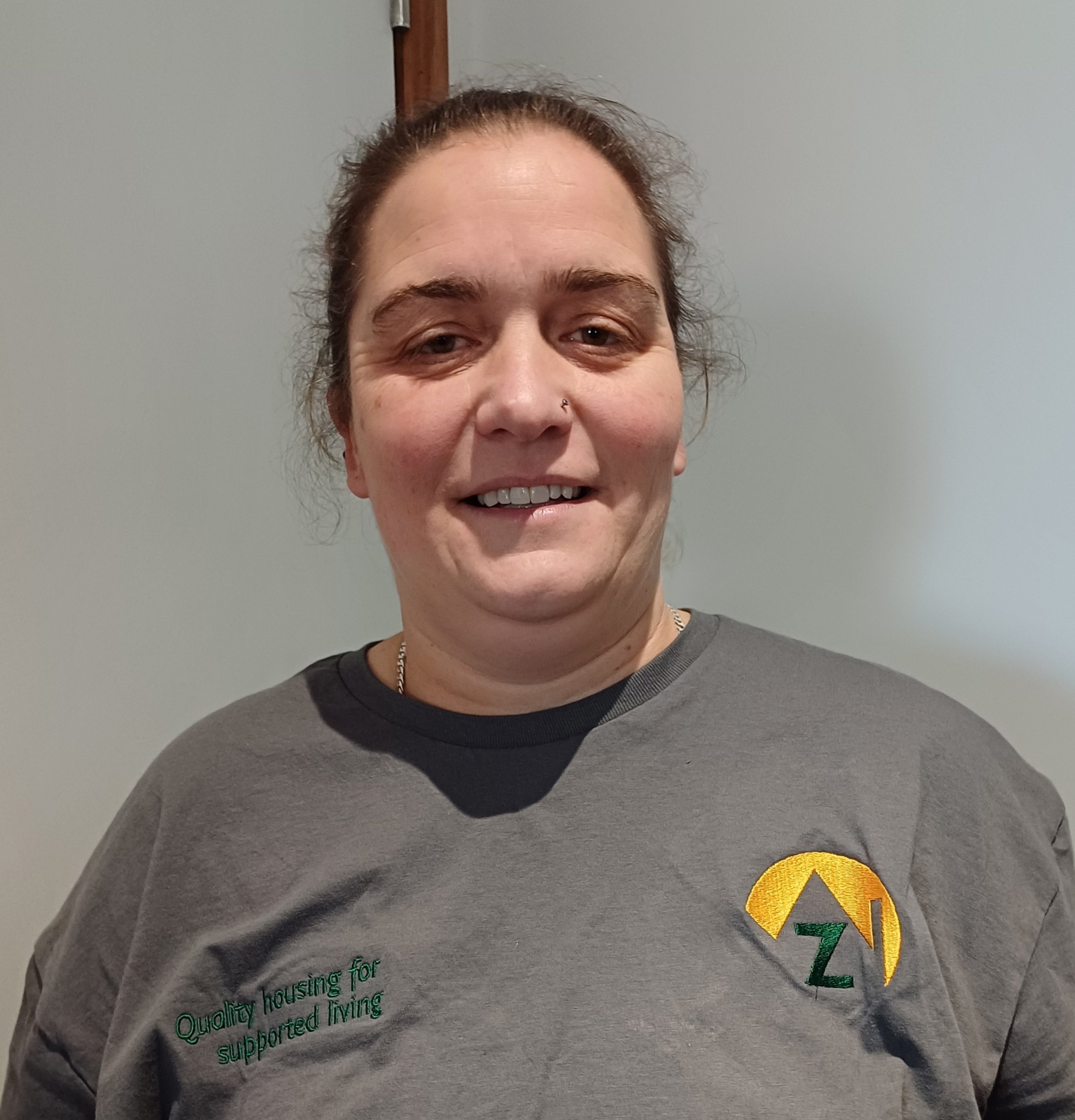 Smiling person wearing branded grey shirt indoors.