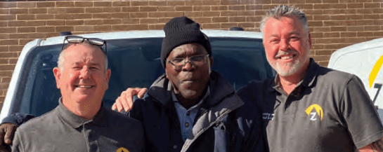 Three men smiling in front of a van.